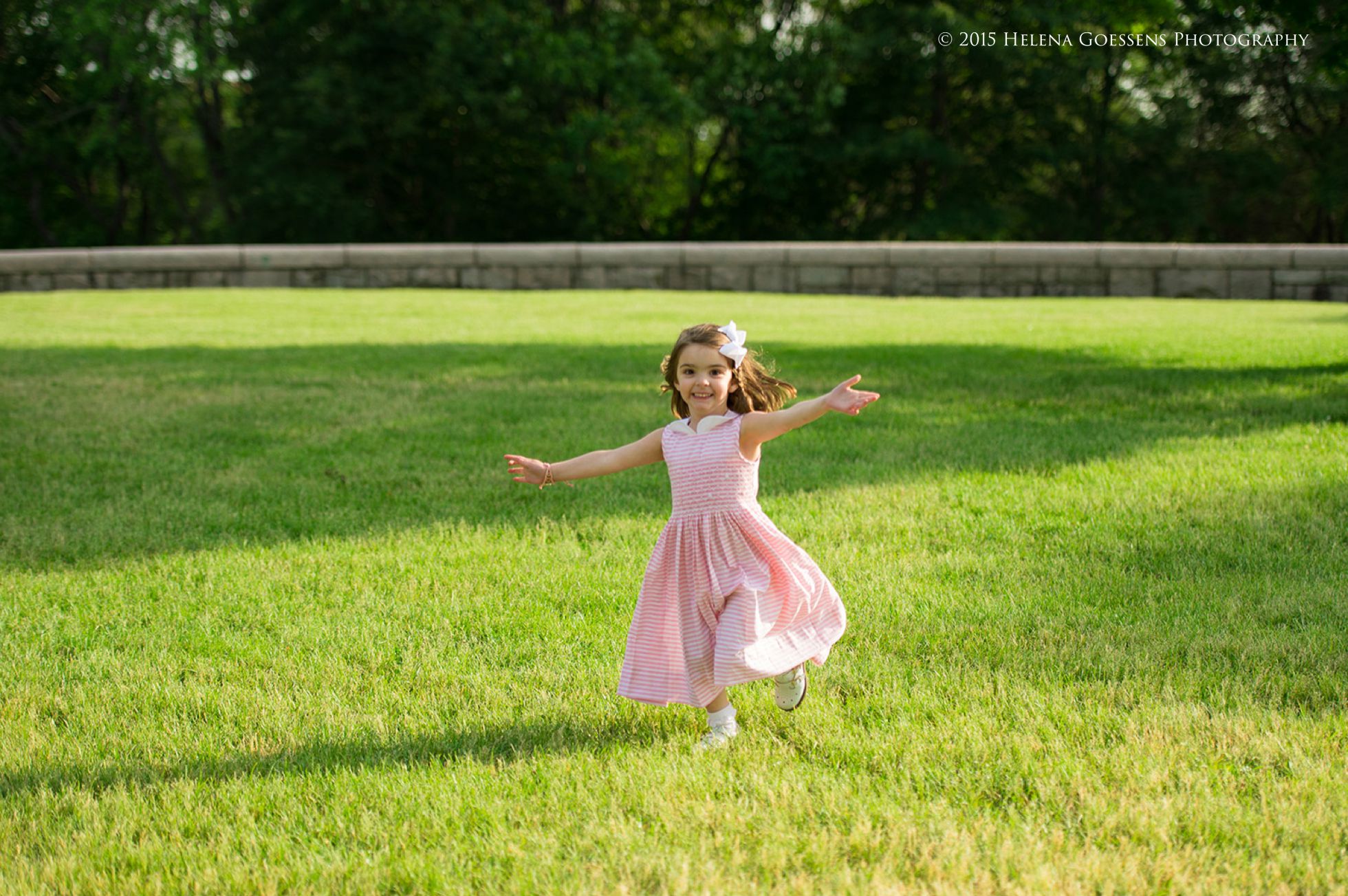 little girl with a pink dress running at the park and looking at the camera