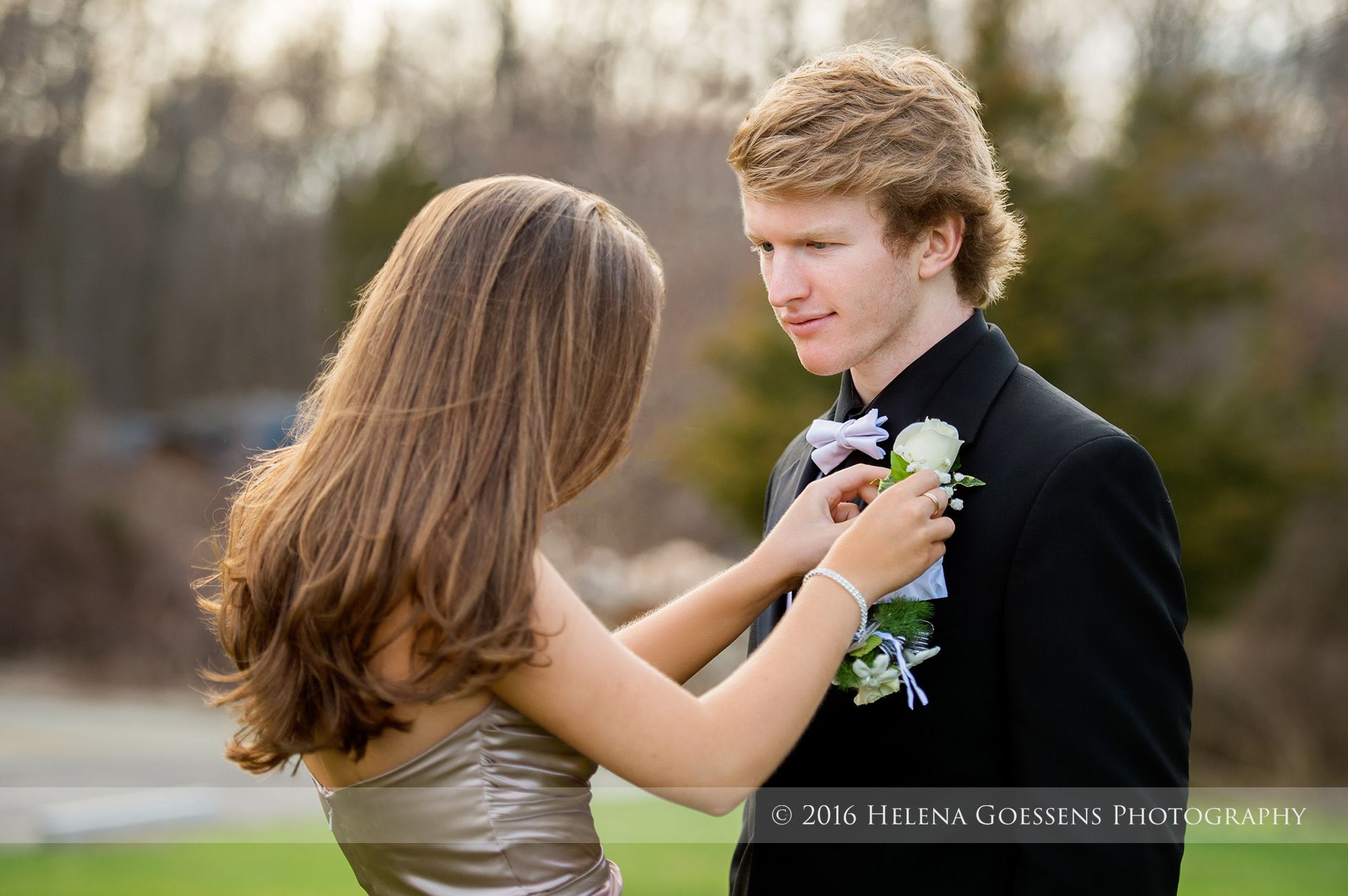 brunette log hair girl attaching a white rose in his tuxedo