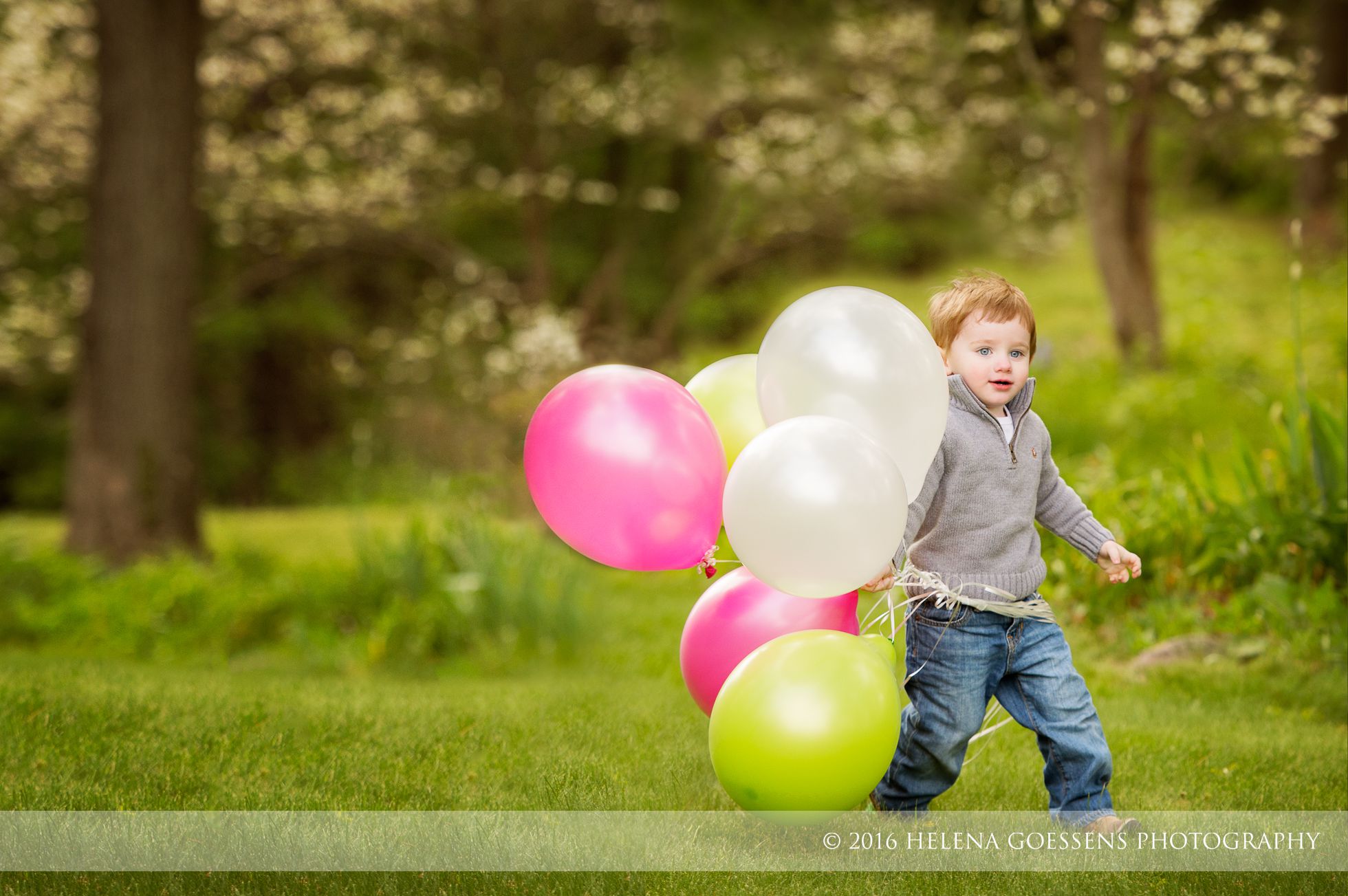 boy wearing a grey pullover running with pink and green balloons.
