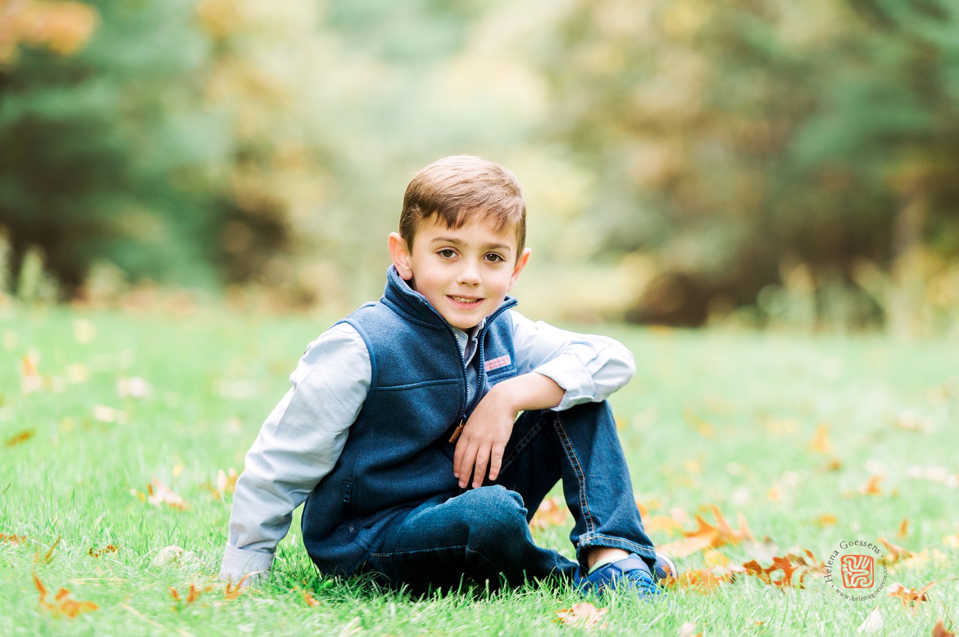 boy in a blue shirt and a blue vest sitting on green grass