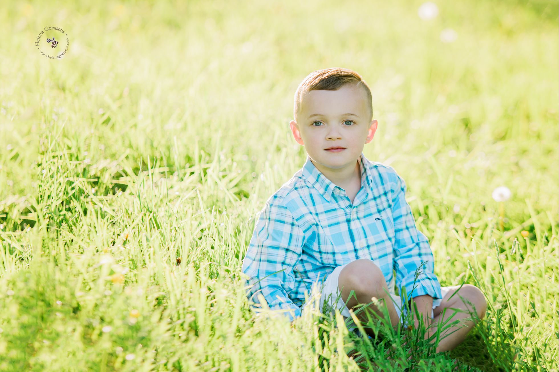 blond boy with blue eyes and a blue shirt sitting on the grass