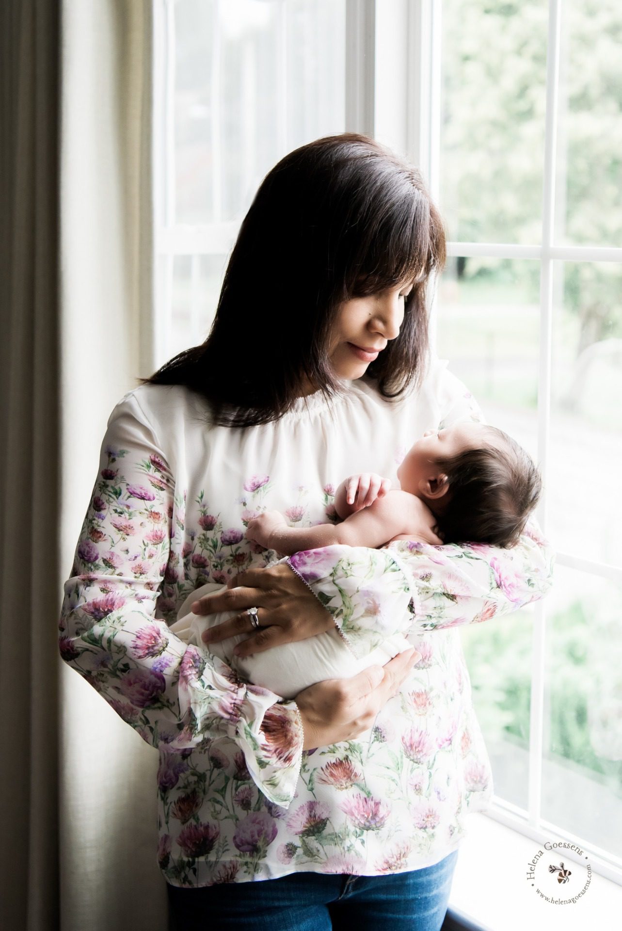 mommy holding her newborn standing next to a window