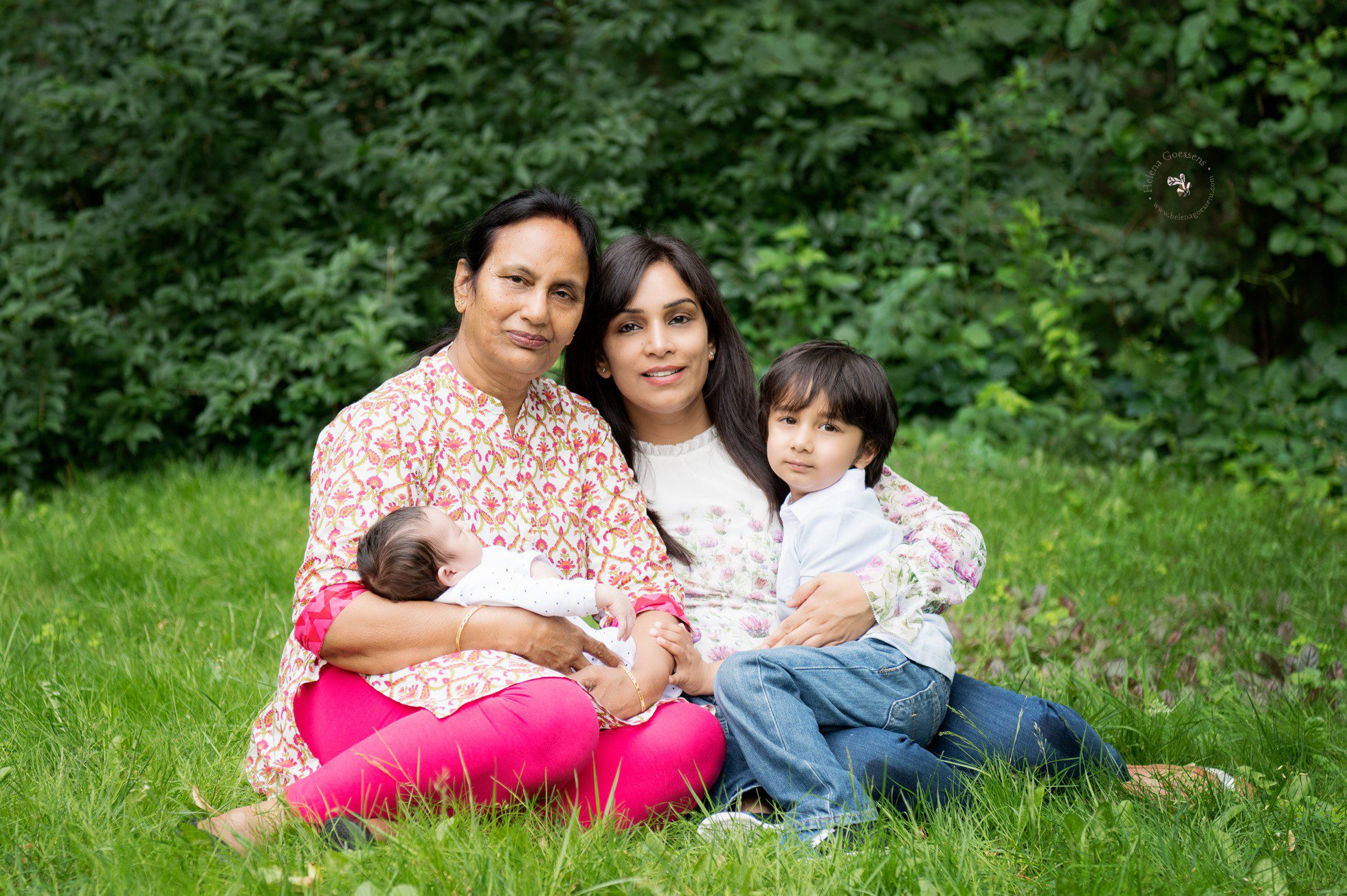 grandmother in pink pants, mom and a baby and a toddler sitting on the grass