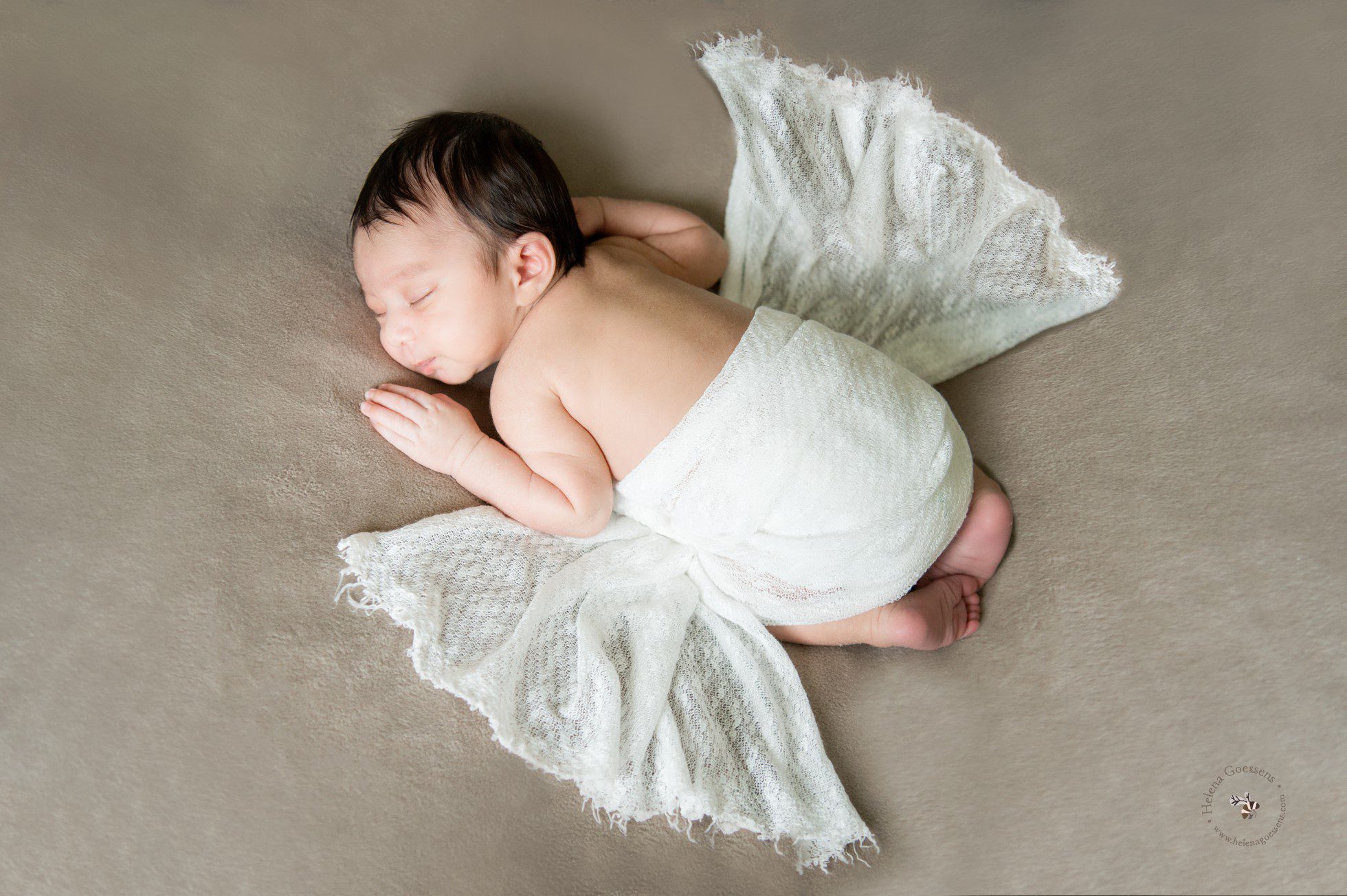 newborn sleeping on his belly and wrapped in white wrap 