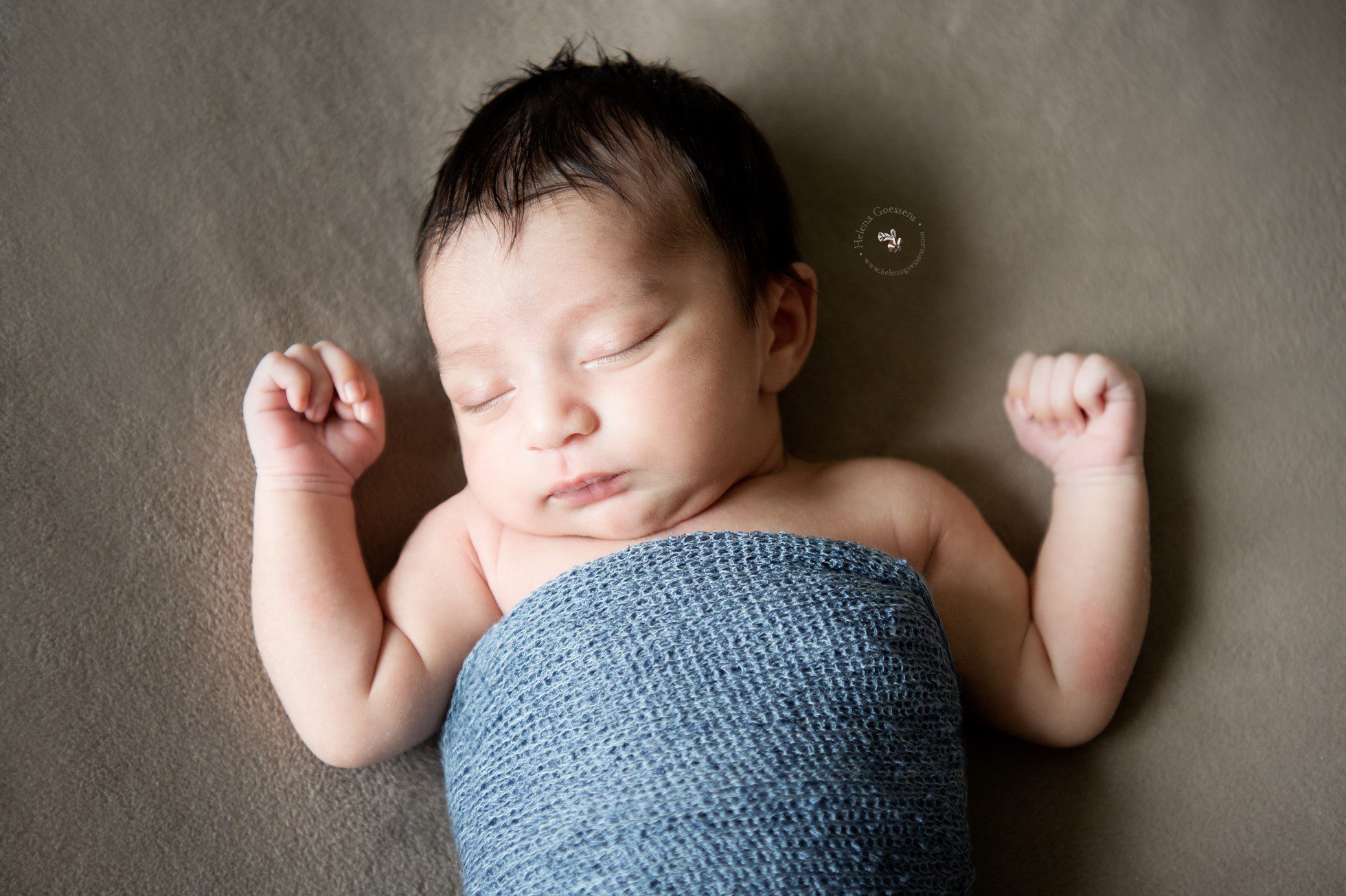 newborn with dark brown hair wrapped in a light blue wrap