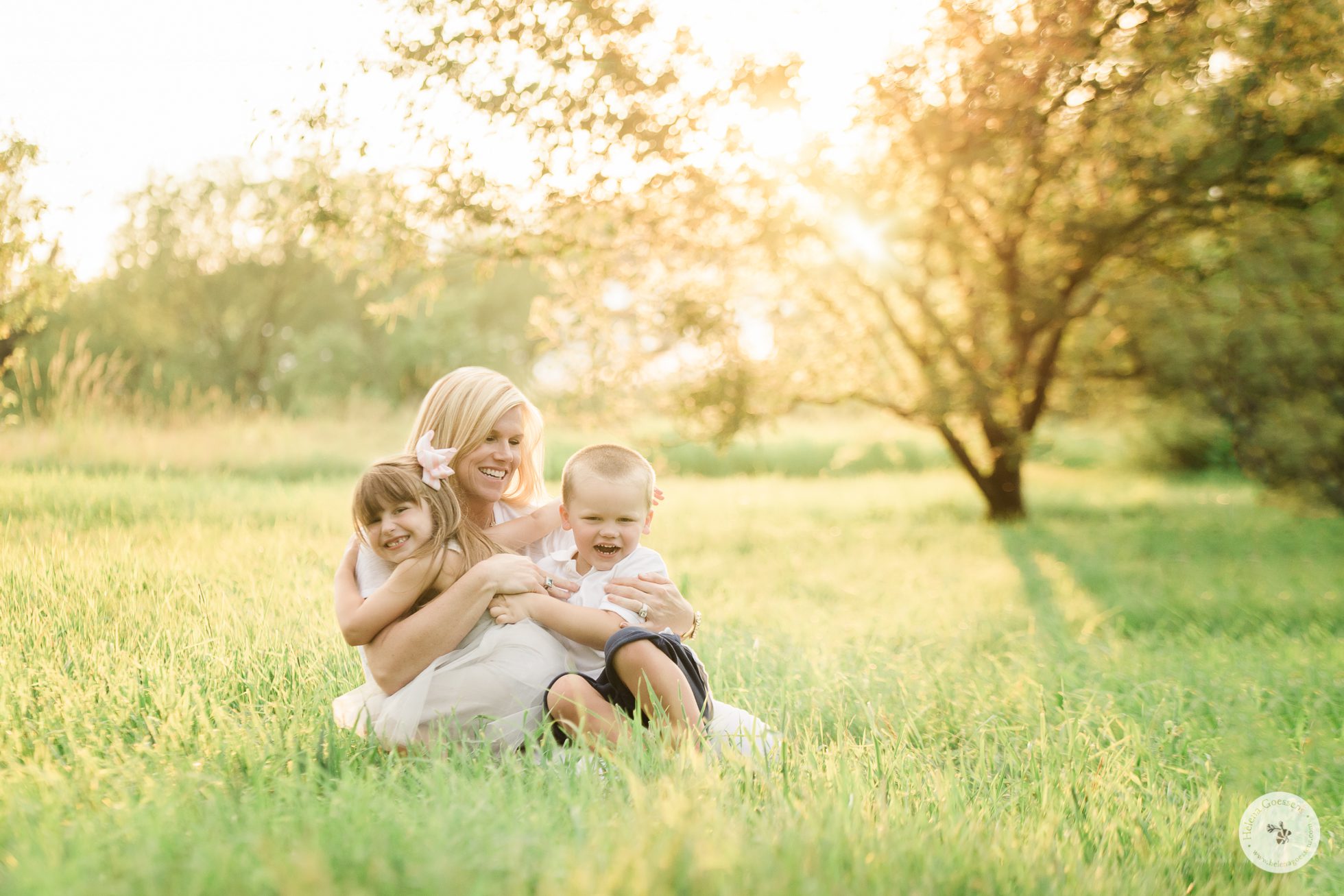 mom sitting on the grass and playing with her two children at sunset. Image by Helena Goessens Photography