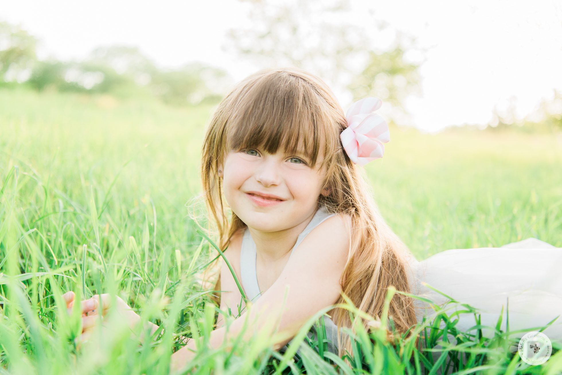 Little girl wearing a big pink bow laying on a green field.