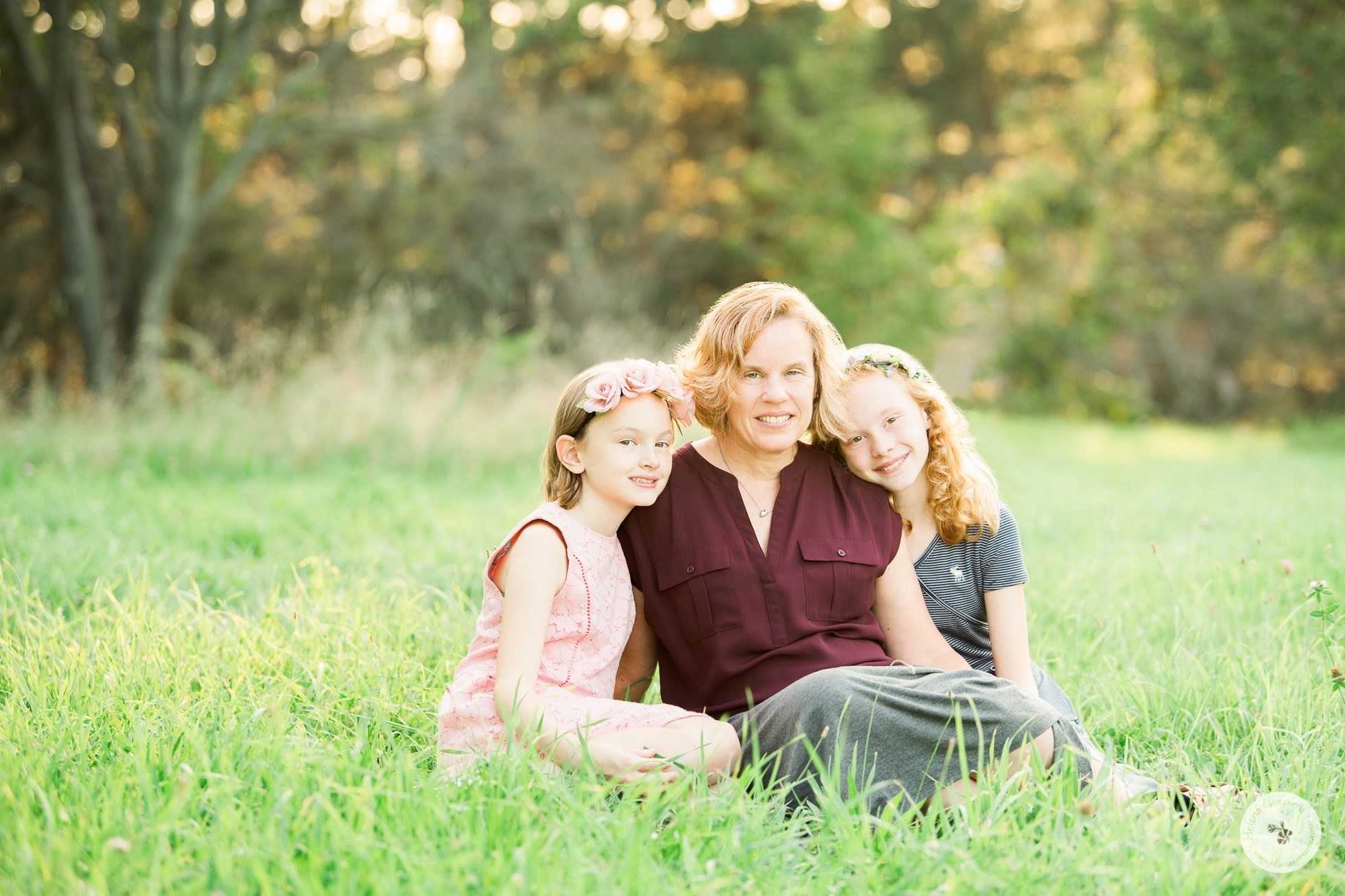 portrait of a mother and her two daughters sitting on a green grass