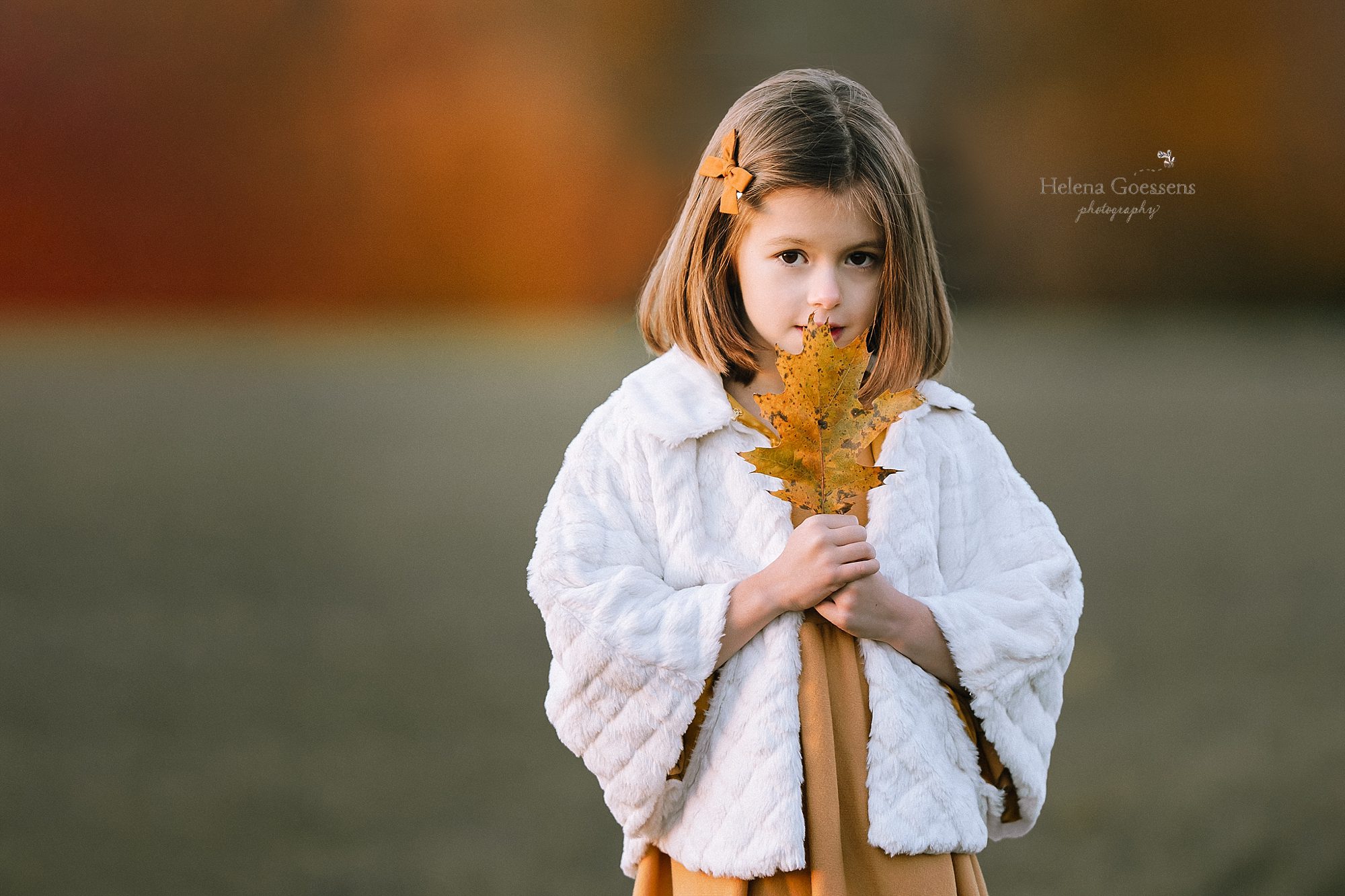 Little girl holds leaf during fall family portraits with Helena Goessens