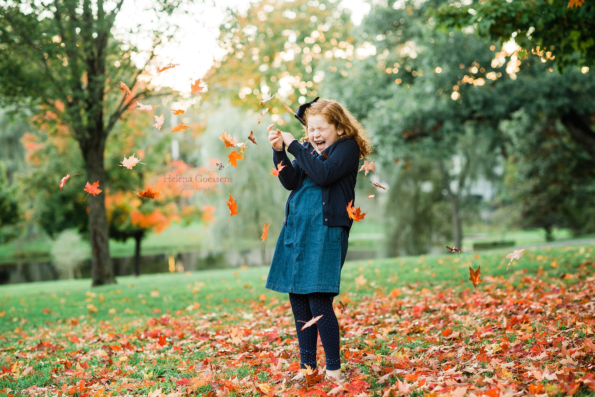 Girl plays in leaves during park family portraits with Helena Goessens
