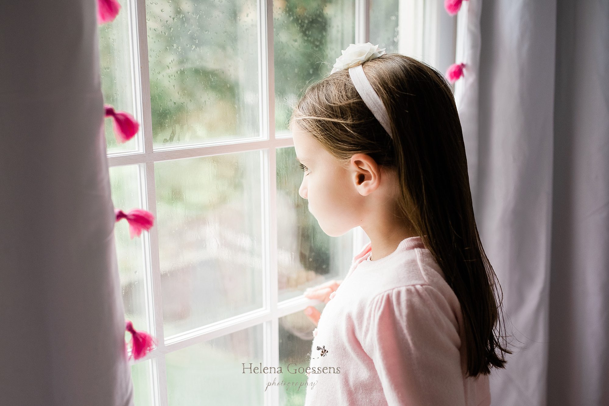 little girl looks out window during session with Helena Goessens Photography
