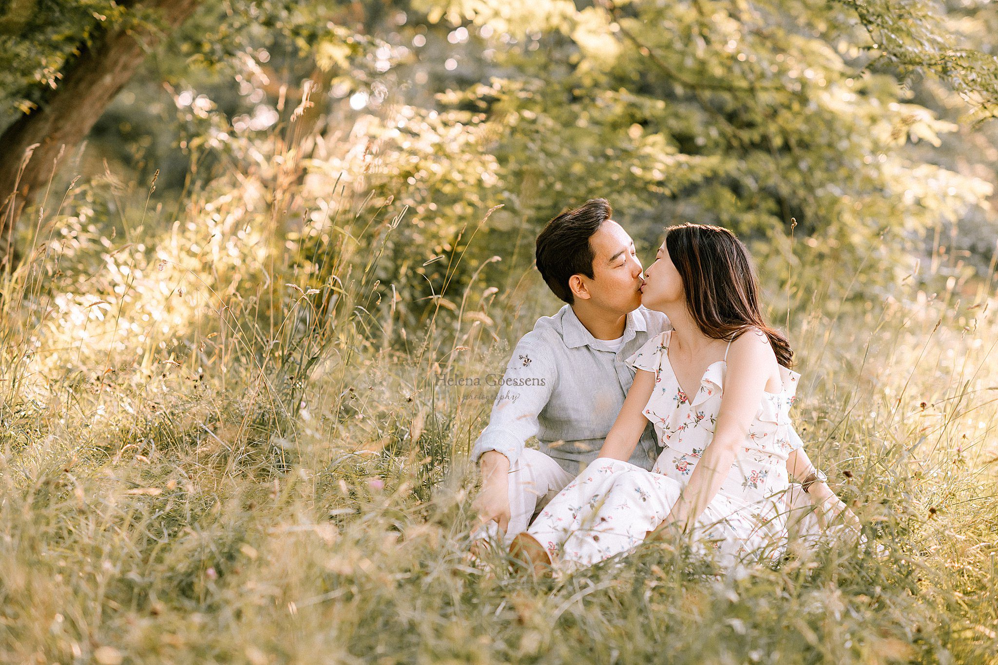 expectant parents kiss in field of Arnold's Arboretum during maternity session with Helena Goessens Photography