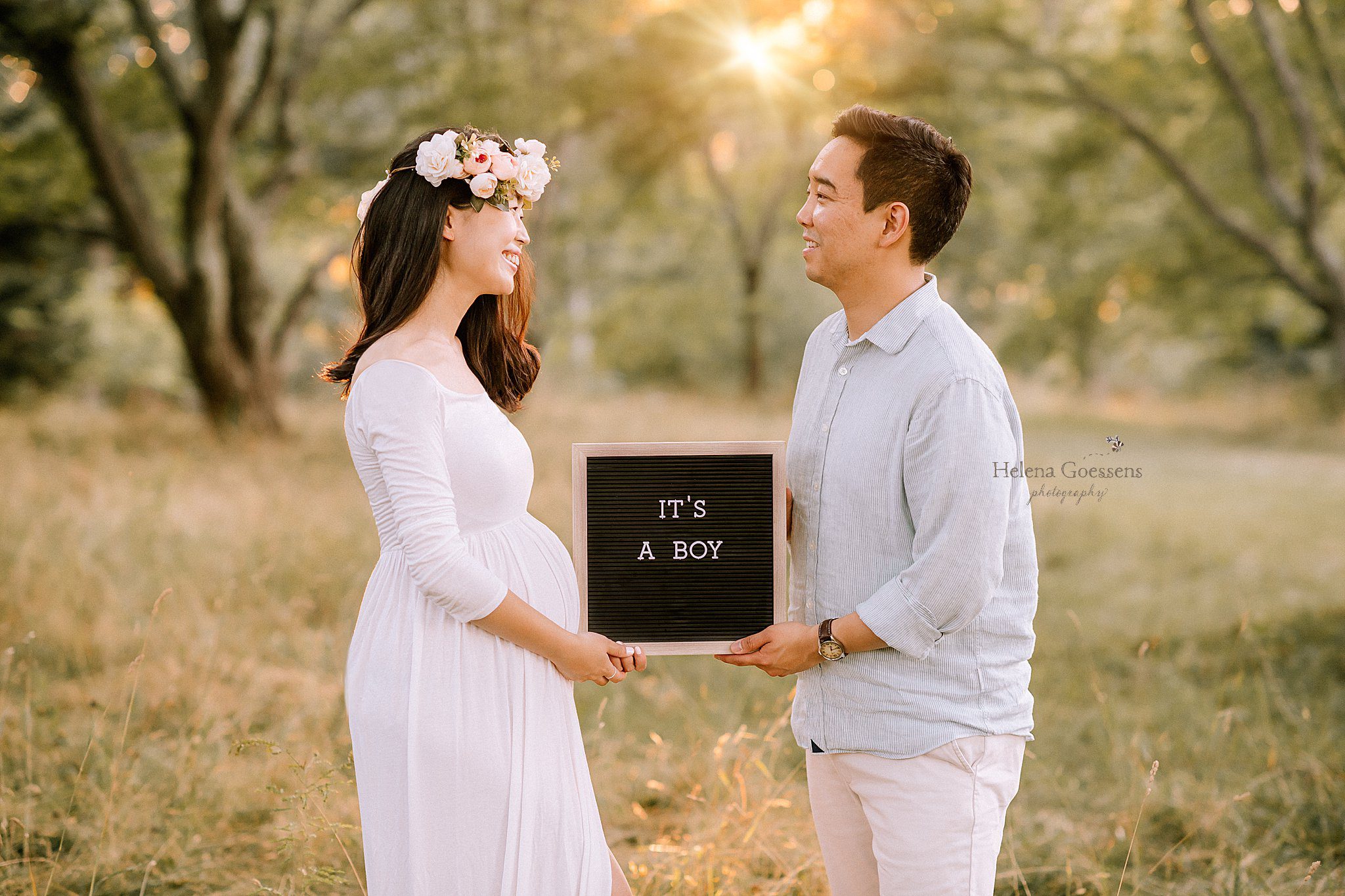 mom in white gown with floral crown holds sign saying "it's a boy" during maternity portraits
