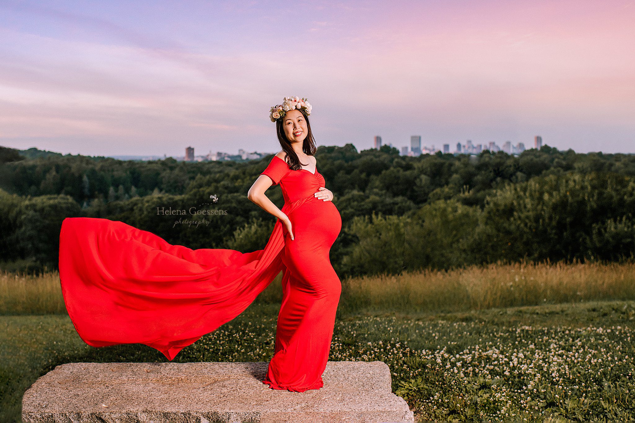 pregnant mom in red dress with flower crown stands in front of Boston skyline