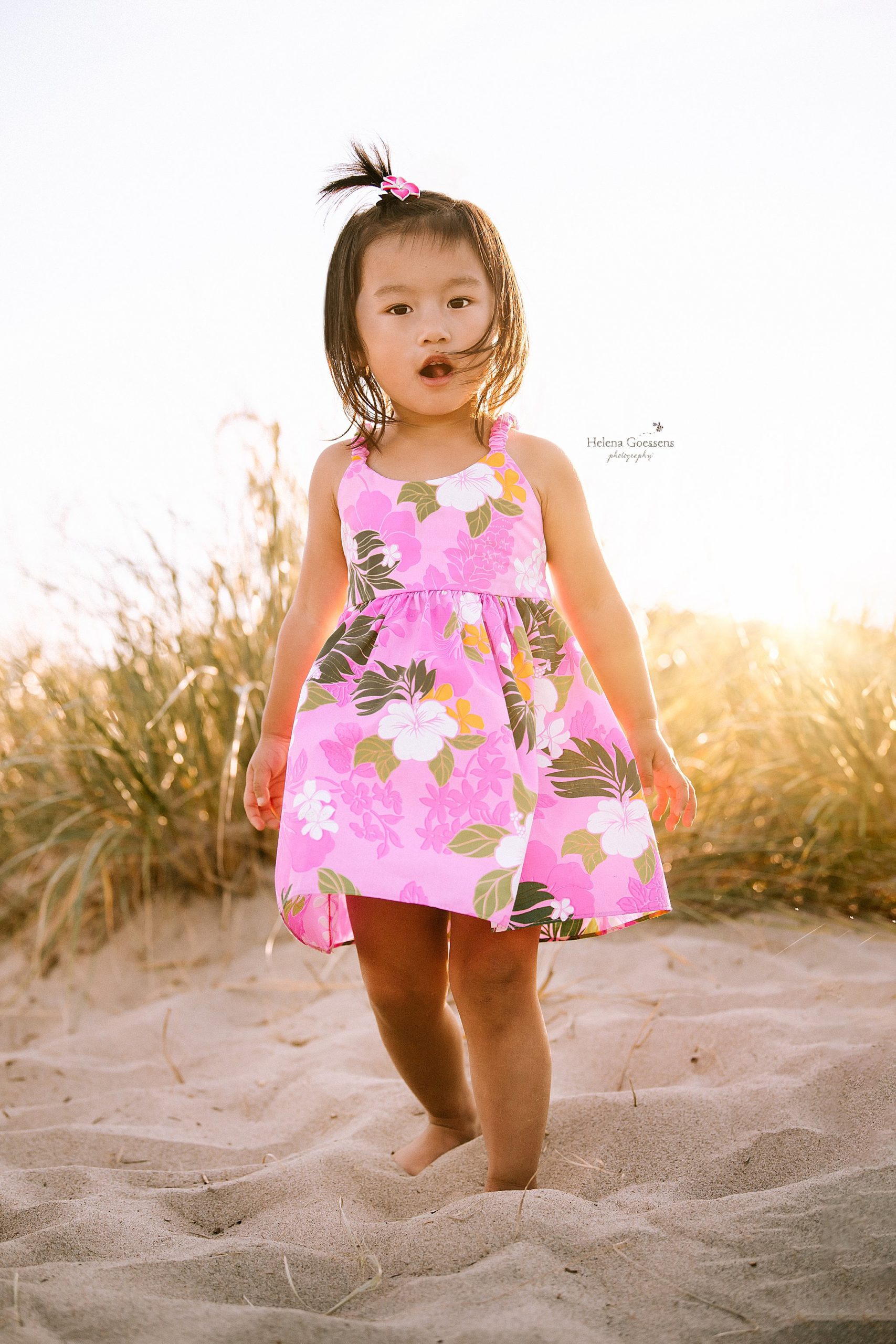 three year old in pink Hawaiian dress runs in sand at Rexhame Beach