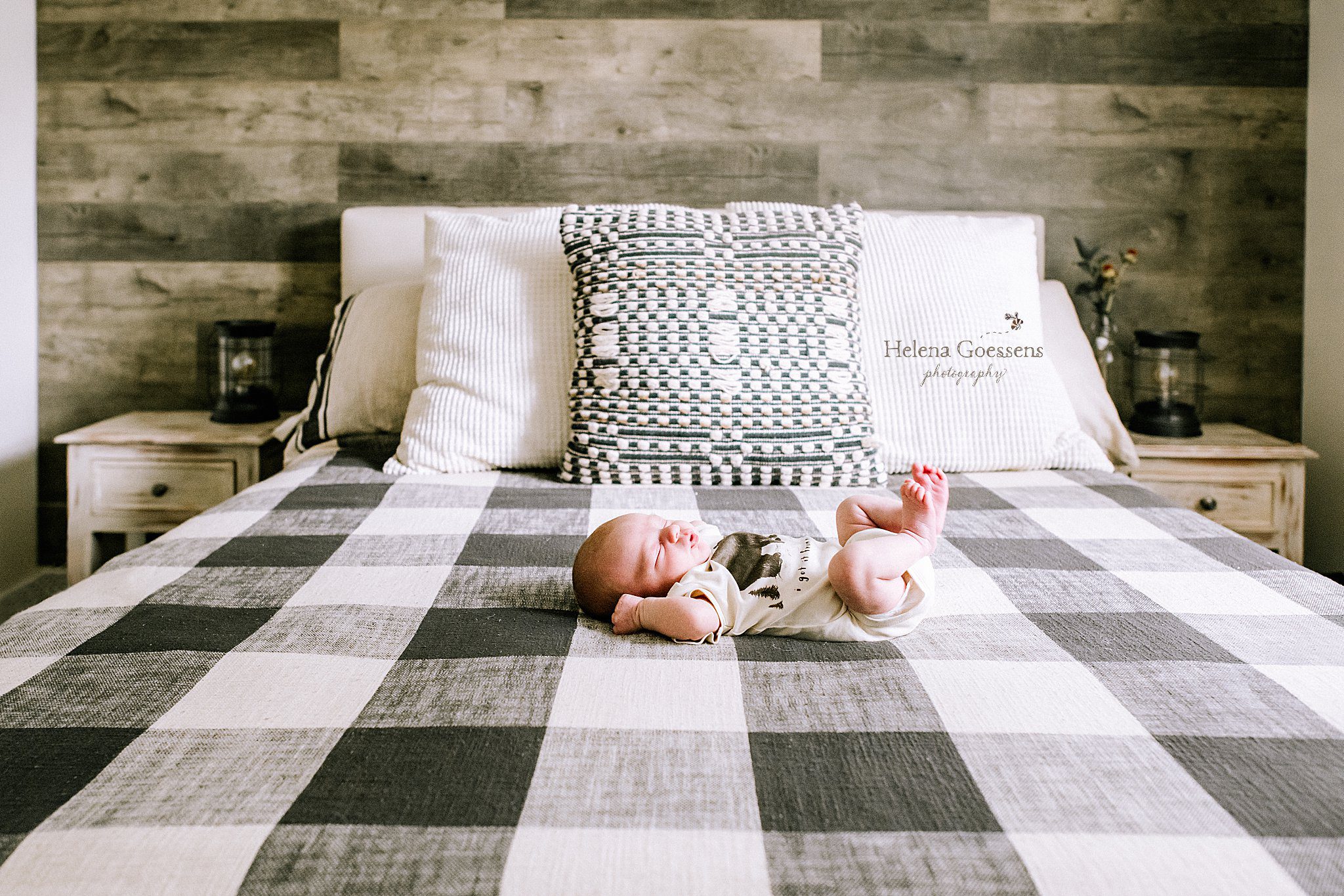 baby boy lays on buffalo plaid bedsheet during lifestyle newborn session with Helena Goessens Photography