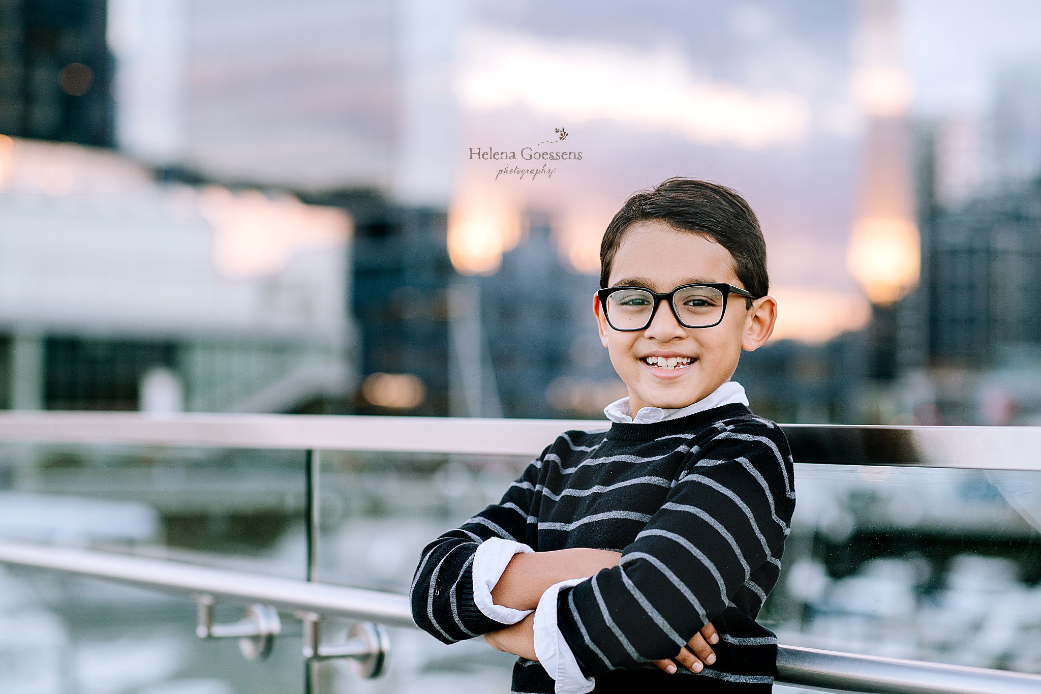 young boy stands with arms crossed with black glasses and a smile