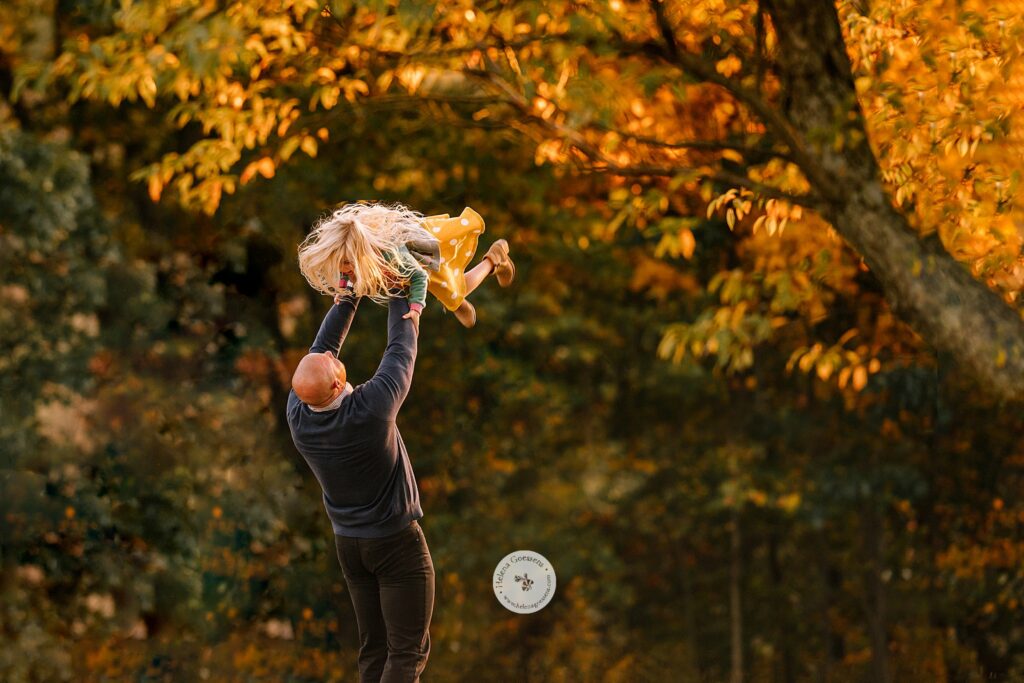 dad lifts daughter up during fall family photos at Larz Anderson Park