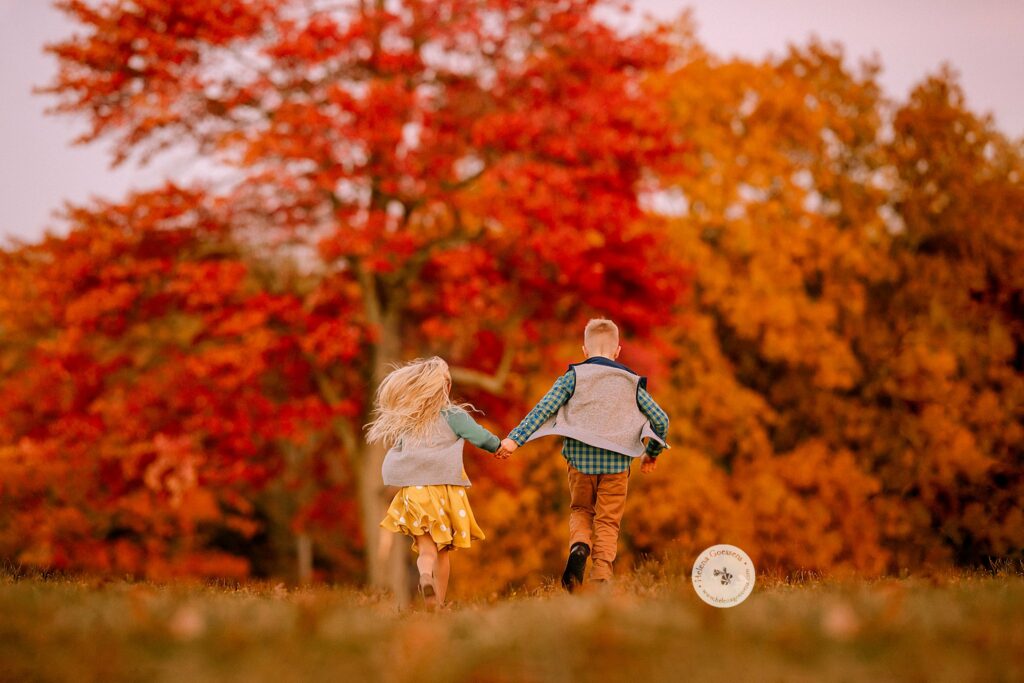 siblings run through field at Larz Anderson Park during Fall Family Portraits in Brookline MA