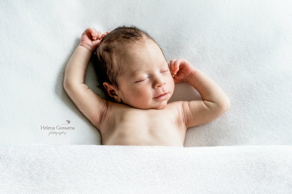 baby lays on bed under white sheets stretching during At Home Newborn Portraits