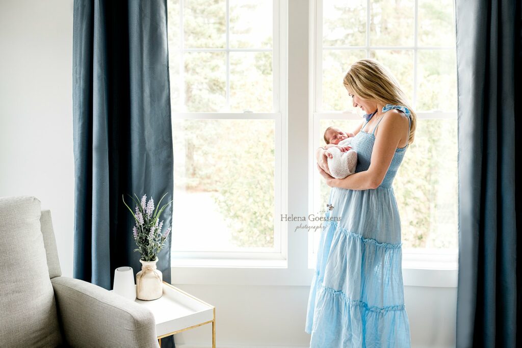 mom in blue dress holds baby boy by window 