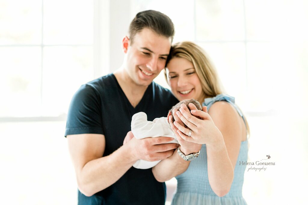 At Home Newborn Portraits with parents holding baby boy and smiling 
