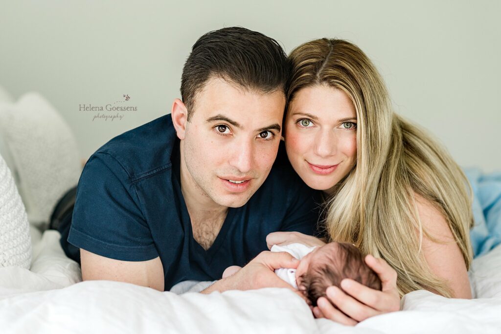 new parents lay on bed cradling baby boy during Needham MA newborn photos 