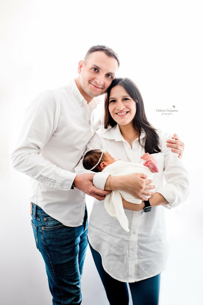new parents in white button down shirts hold baby girl during newborn session