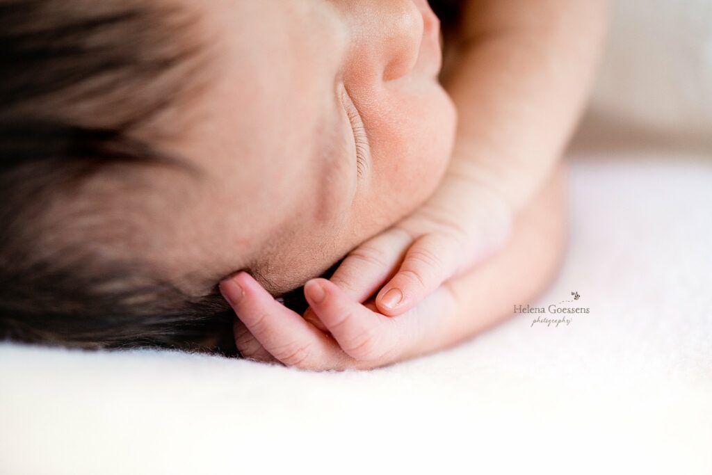 baby lays with hands under her head during newborn photos at home 