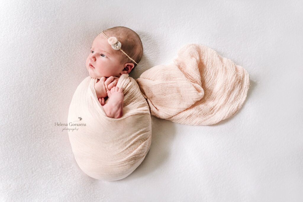 baby lays in pale pink wrap on bed during Lifestyle Newborn Session in Quincy MA