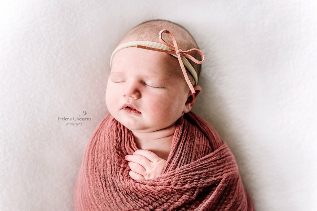 baby sleeps in rose wrap with headband on during newborn photos 