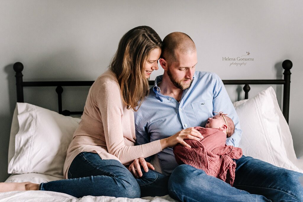 parents look down at baby girl during newborn photos at home 