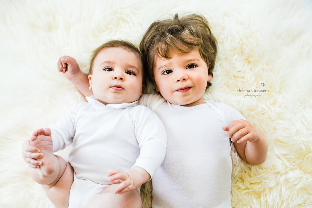 brothers lay on rug in simple white onesies during Lifestyle Family Portraits in Weston MA
