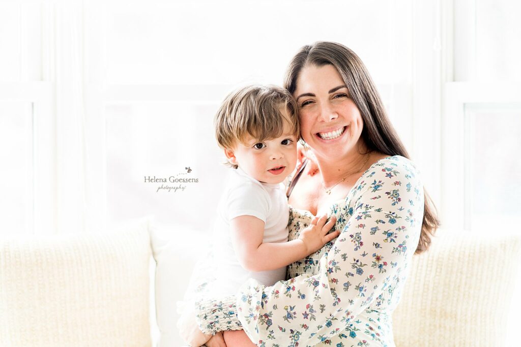 mom in floral print gown hugs son on the couch during Lifestyle Family Portraits in Weston MA