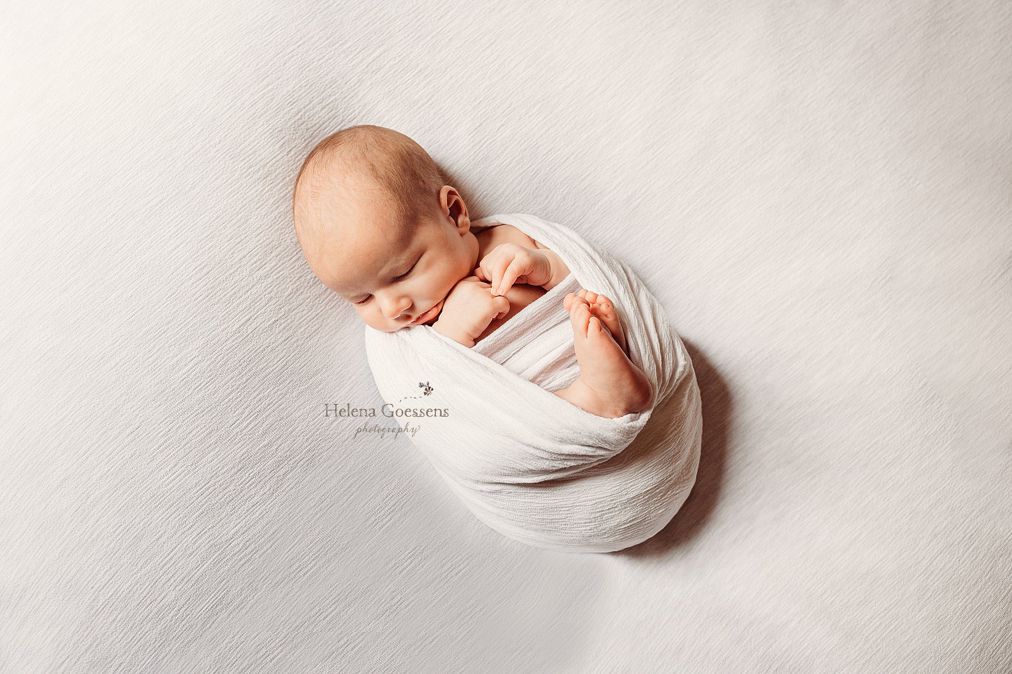 baby in white wrap lays on couch during newborn portraits at home in Boston 