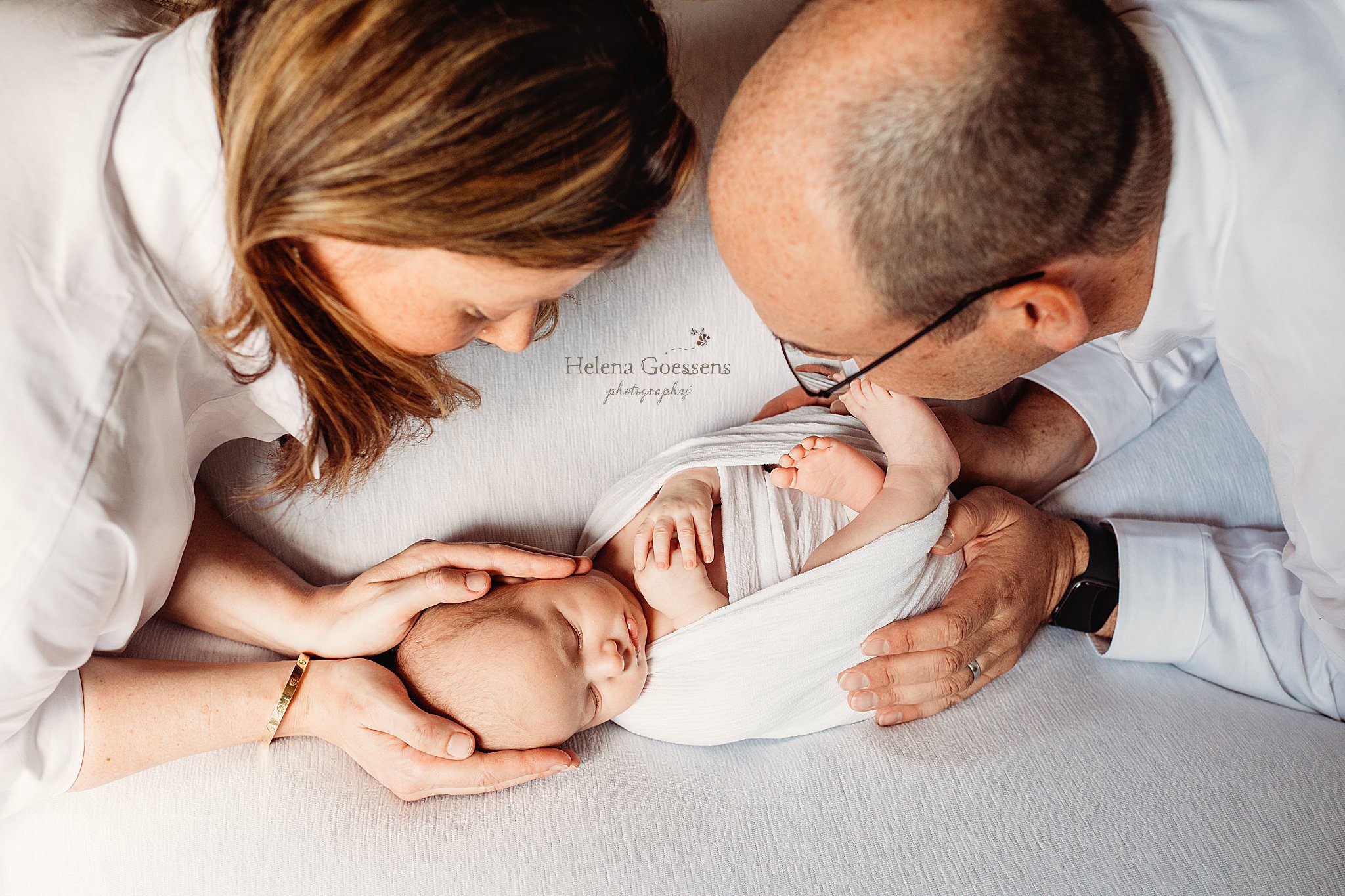 parents look down at baby boy in white wrap during South End newborn session at home 