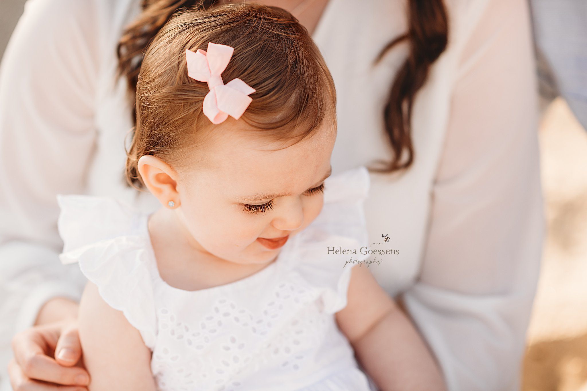 baby girl looks at sand with pink bow in hair during Rexhame Beach family session