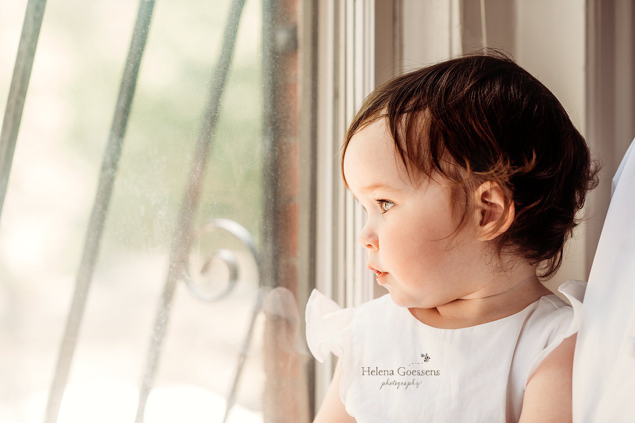 toddler girl looks out window during family photos at home 