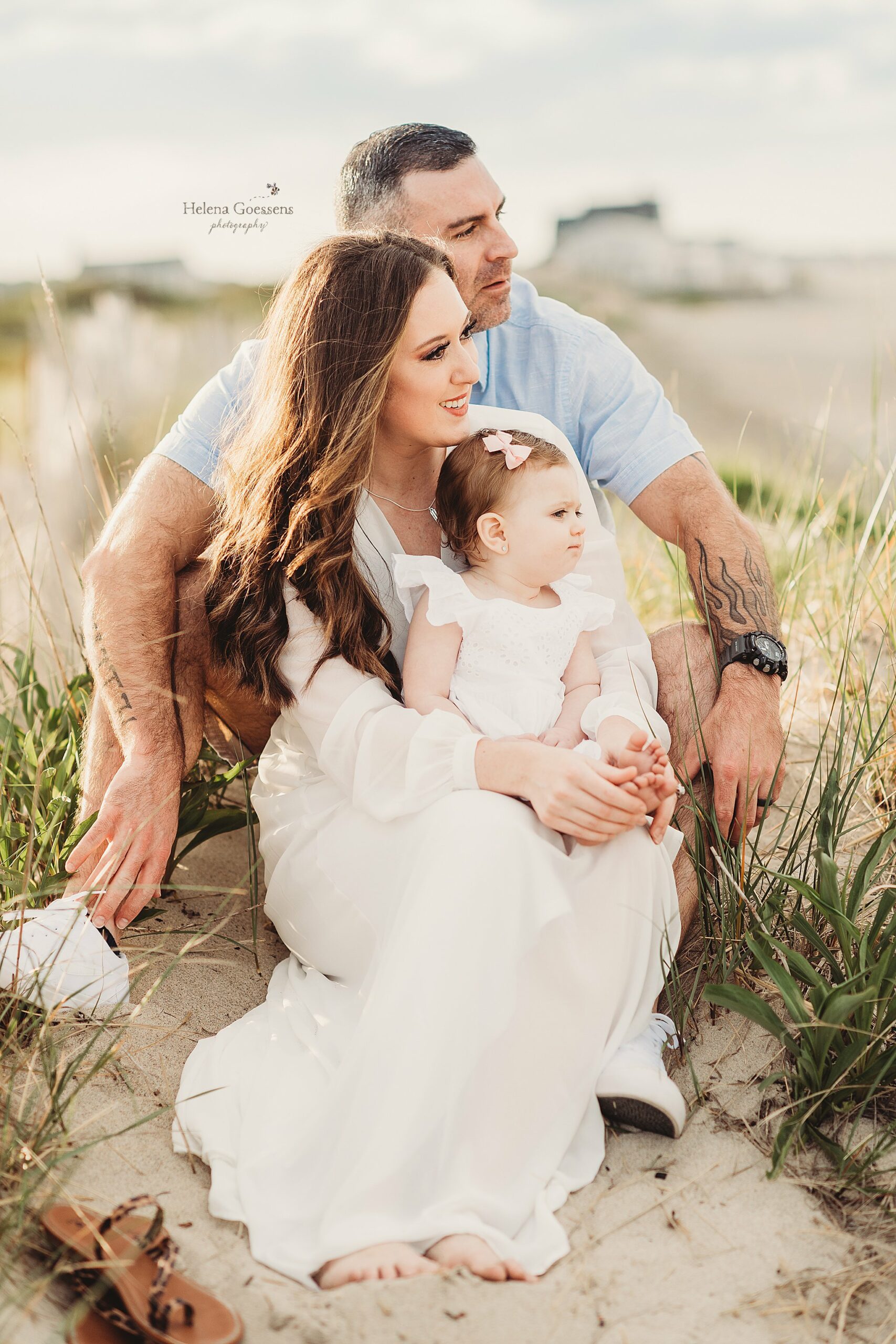 parents and toddler sit in tall grass looking at ocean during Rexhame Beach family session