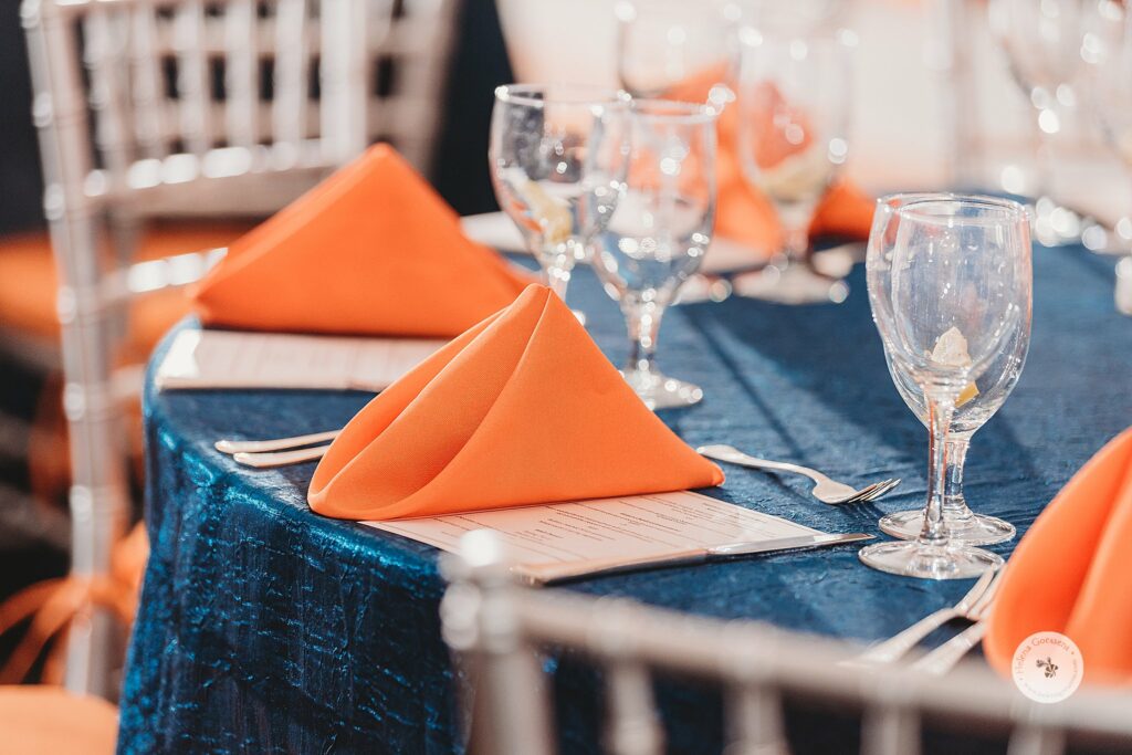place settings with orange napkins on blue tablecloth in MA