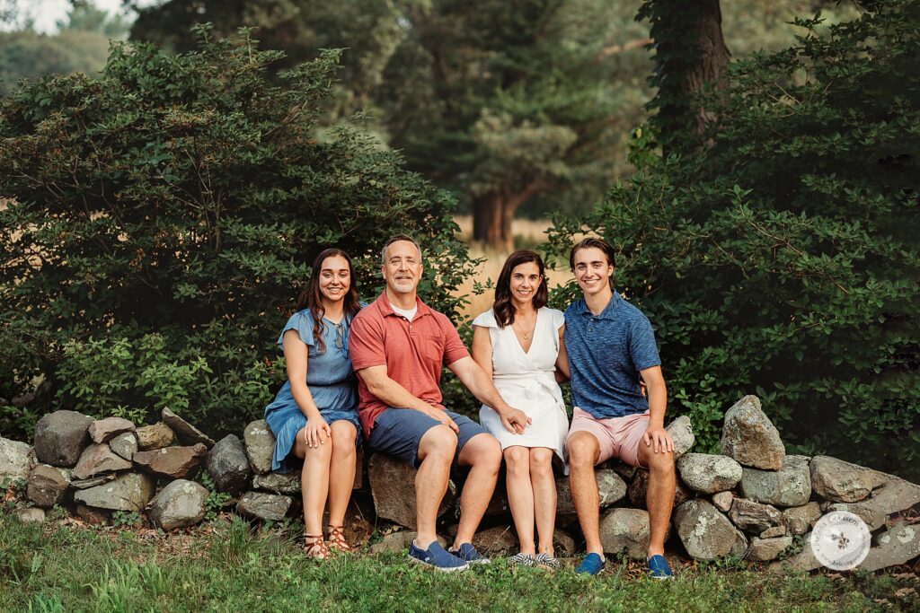 family of four sits on rock wall during Bradley Estate Family Photos