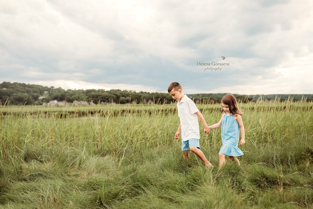 siblings hold hands walking through dunes in Marshfield MA 