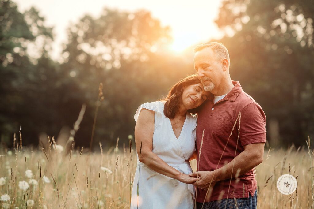parents lean together during Bradley Estate Family Photos in the tall grass at sunset 
