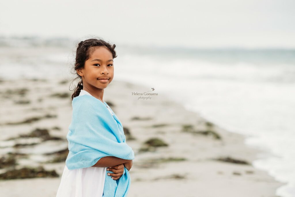 girl stands with blue shawl around shoulders during family photos on Rexhame Beach