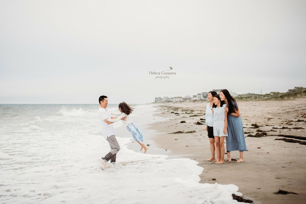 dad plays with daughter in water during family photos on Rexhame Beach