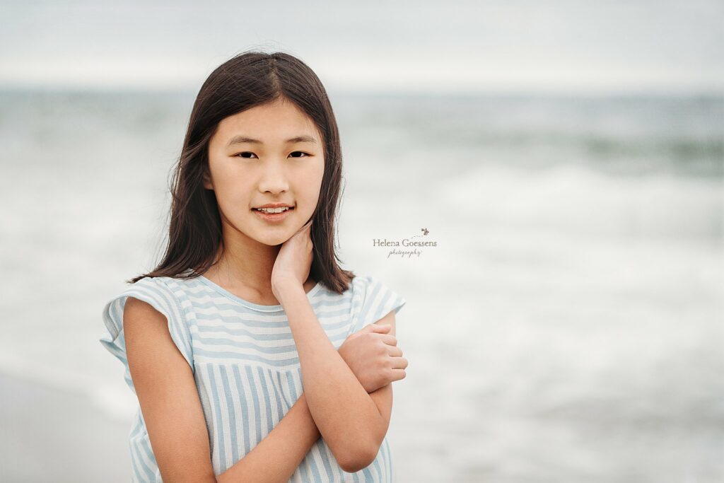 girl stands with hand resting on neck in front of ocean during Extended Family Portraits at Rexhame Beach