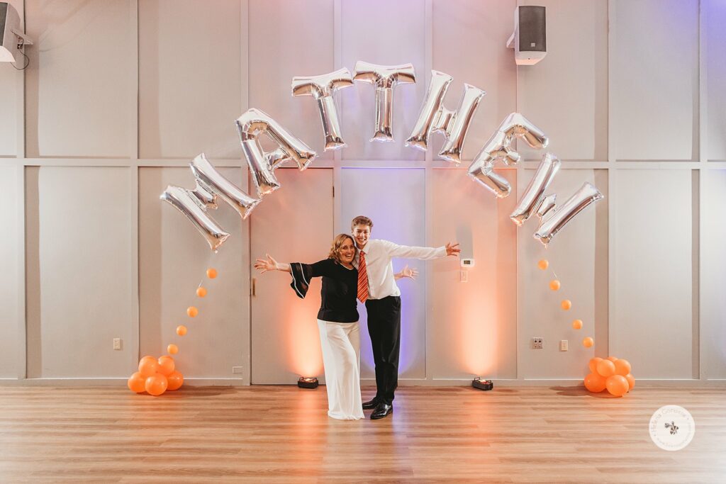 son and mom pose under "Matthew" balloons during Bar Mitzvah at the Temple Beth Avodah