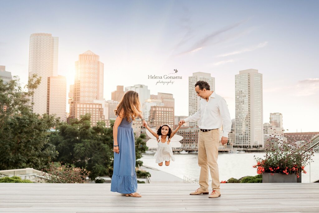 parents wing toddler in fairy wings with Boston skyline behind them 
