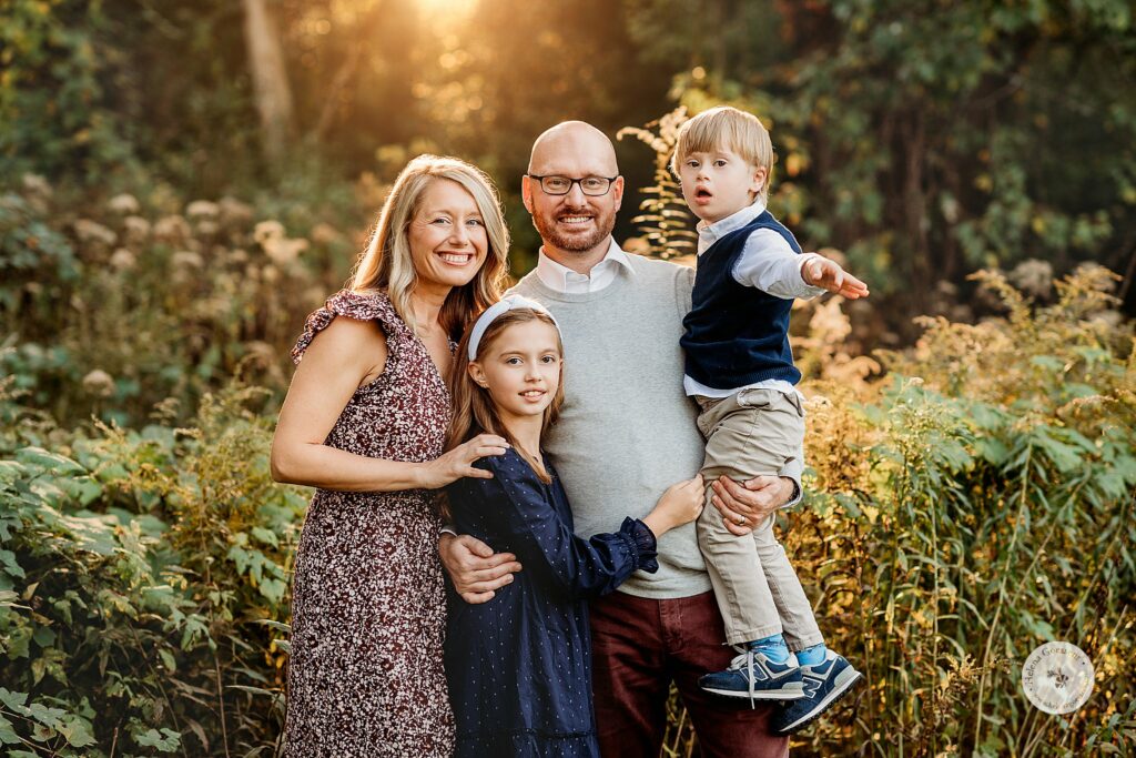family of four hugs in tall grass during fall family portraits at Larz Anderson Park