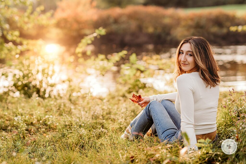 senior girl sits by water holding leaf at The Old Manse